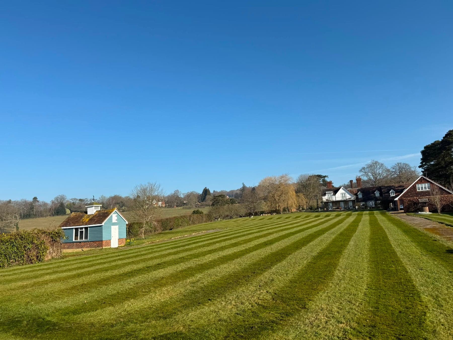 A large garden lawn with alternating mower stripes, showing the visible result of grass cutting and lawn maintenance.
